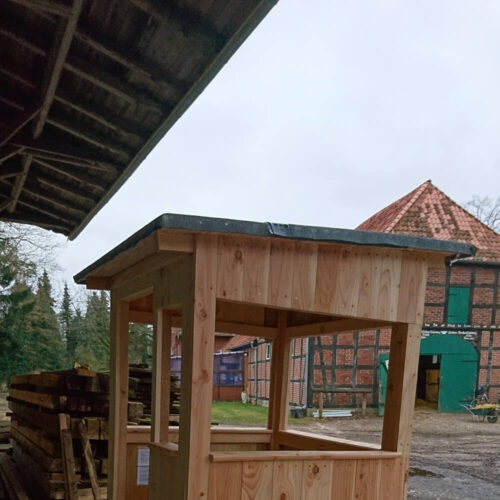 Offene Jagdkanzel Waidmann aus Holz auf einem Bauernhof mit Scheune im Hintergrund