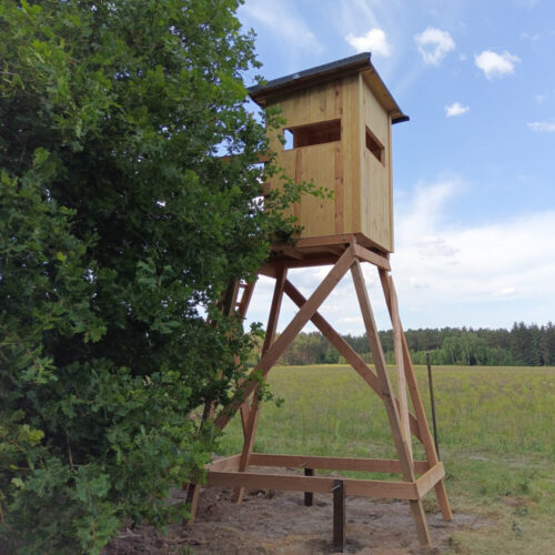 Offene Jagdkanzel Waidmann auf Holzgestell in grüner Wiese mit blauem Himmel