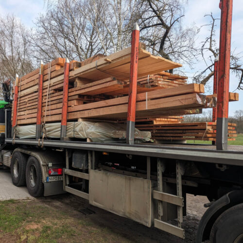 Ein Lastwagen transportiert große Mengen von Schnittholz und Schwartenbrettern. Die Holzladung ist fest verzurrt.