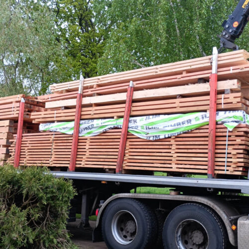 Ein Lastwagen transportiert große Stapel von Schnittholz und Schwartenbrettern, teilweise mit einer grünen Abdeckung.